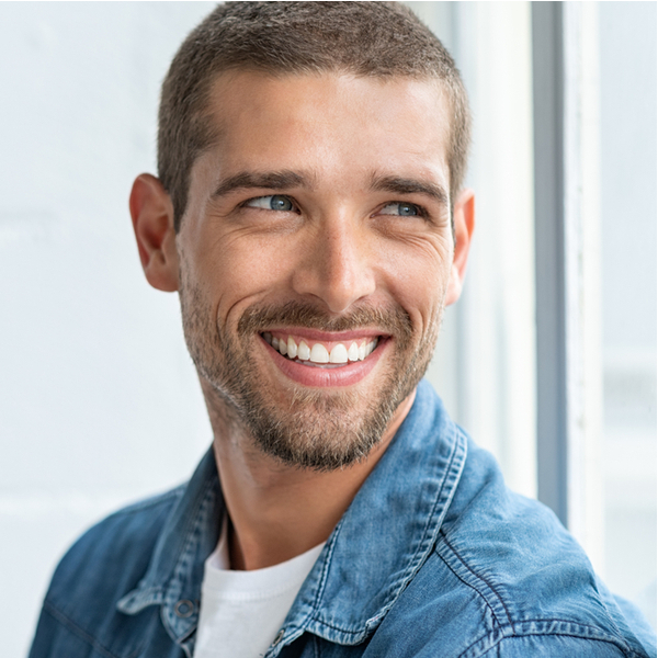 Man smiling and looking away from the camera with a light interior of a Dallas dentist's office in the background.
