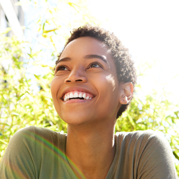 A smiling woman looking upward with sunlight casting a glow on her face after visiting an affordable Dallas dentist.