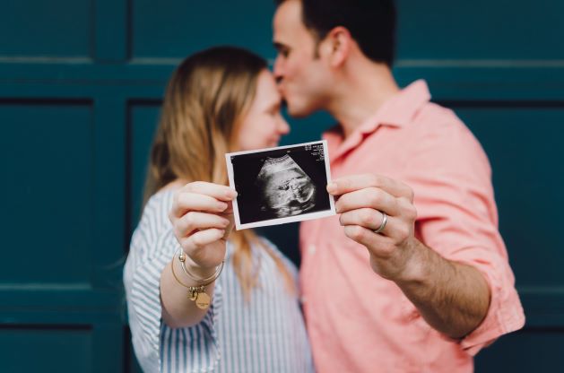 Couple holding an ultrasound image while sharing a kiss after their appointment with an affordable Dallas dentist.