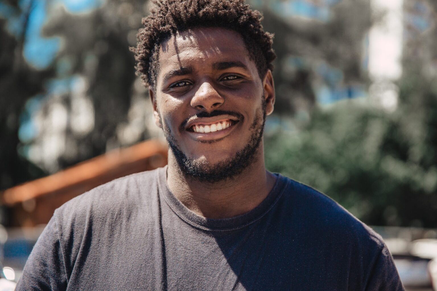 A cheerful man with a beard and curly hair, smiling outdoors after visiting his Dallas dentist.