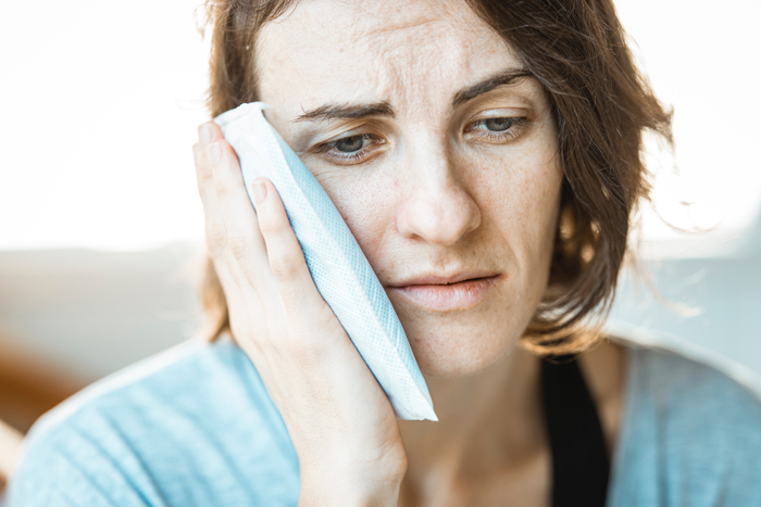 Woman holding ice pack to her cheek to alleviate pain after visiting an affordable Dallas dentist.