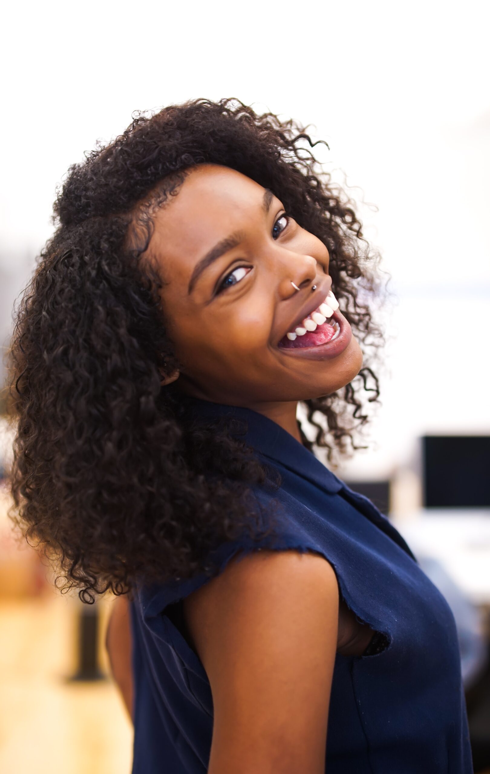 A cheerful young woman with curly hair smiling at the camera, reminiscent of the bright smiles crafted by an affordable Dallas dentist.