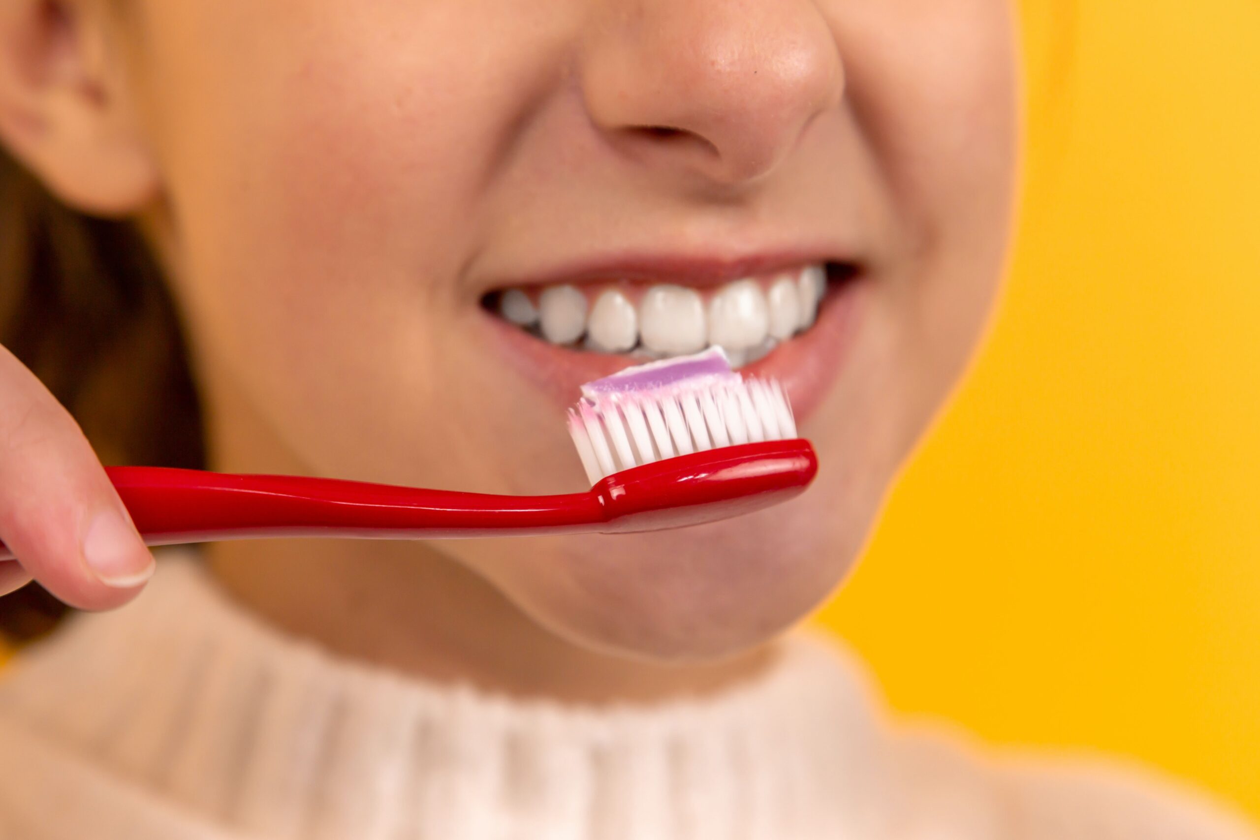 Close-up of a person brushing teeth with a red toothbrush at an affordable Dallas dentist office.