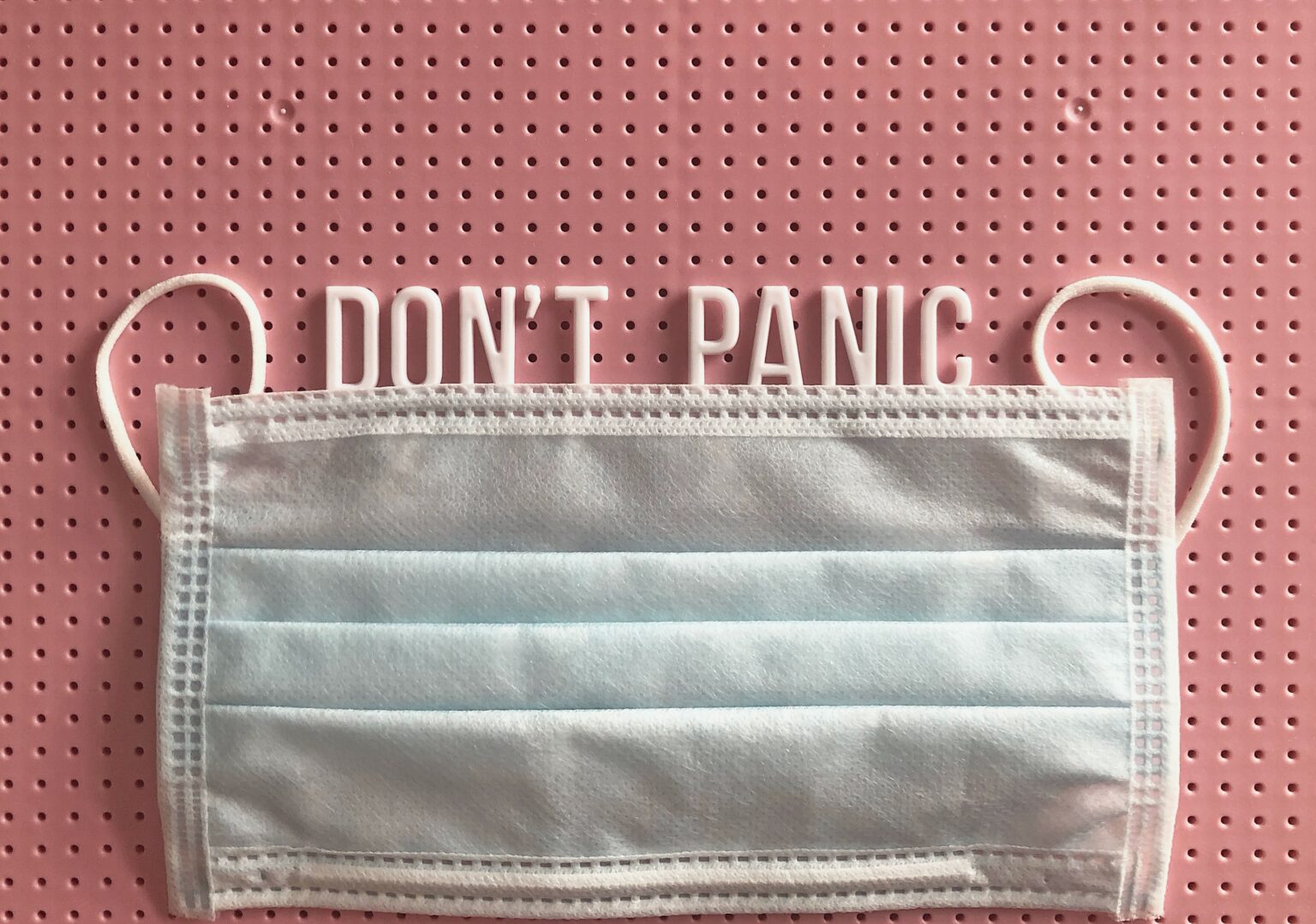 A surgical mask placed above the phrase "don't panic" spelled out on a pink pegboard at an affordable Dallas dental clinic.