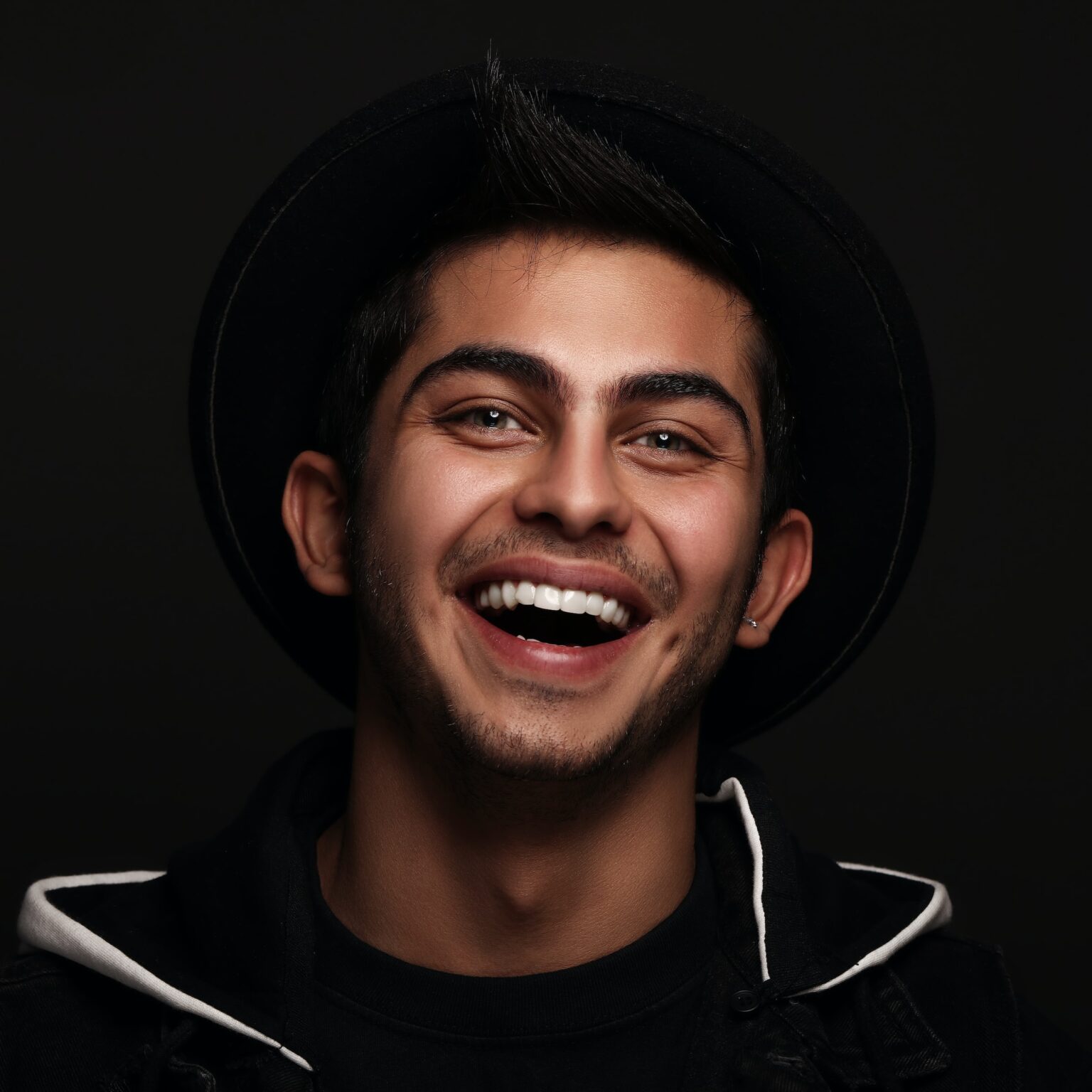 A smiling young man wearing a black hat against a dark background of a Texas dentistry office.
