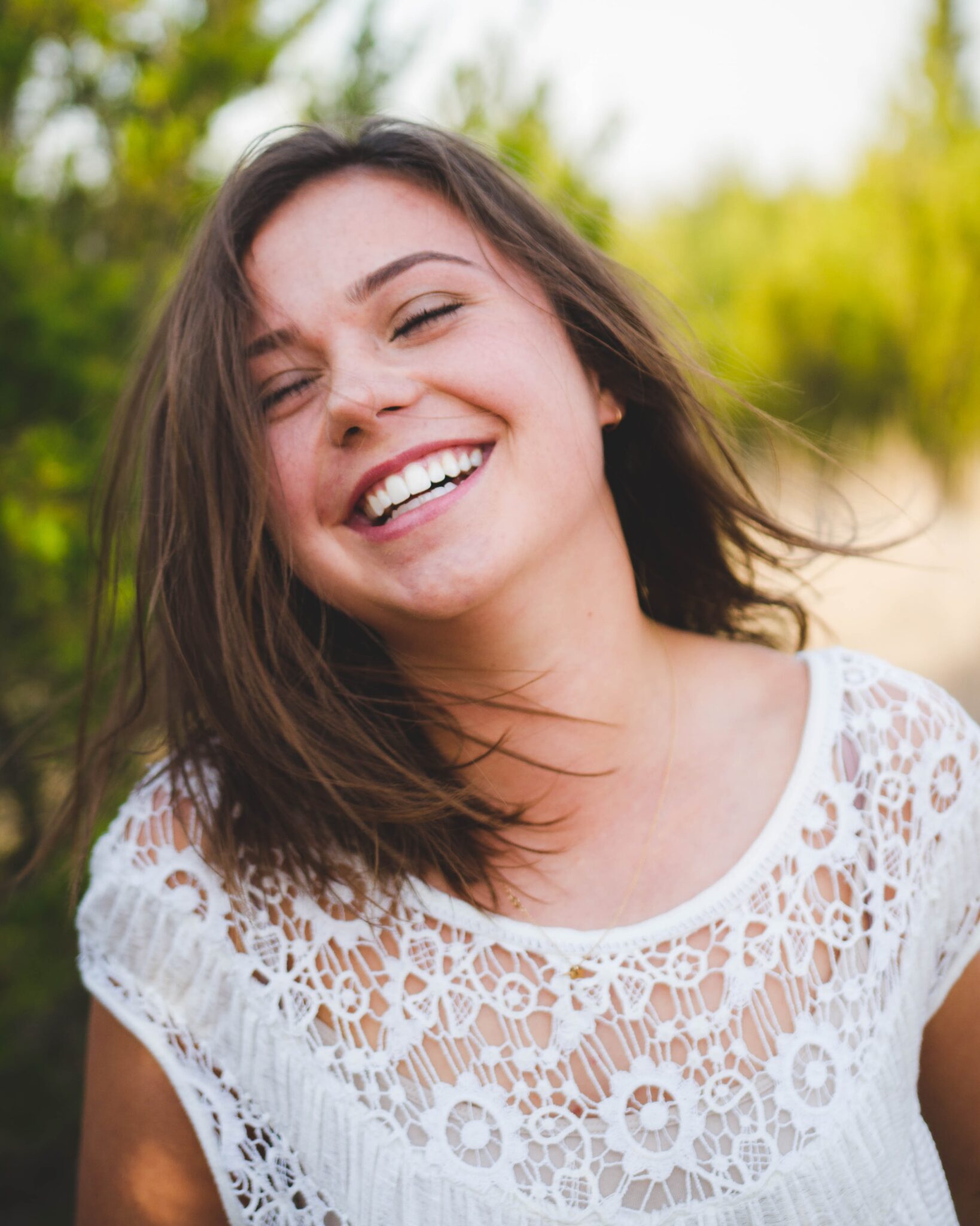 A woman smiling joyfully, showcasing her perfect teeth treated by a Dallas dentist, in a natural setting.