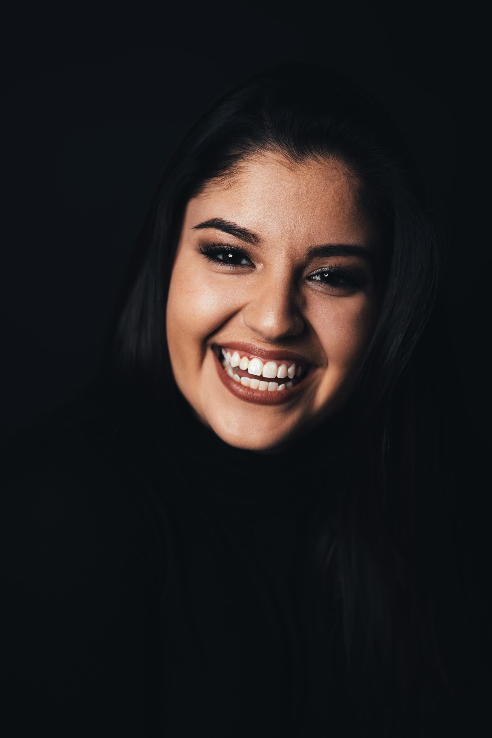 Woman with a bright smile, enhanced by her dentist in Dallas, posing against a dark background.