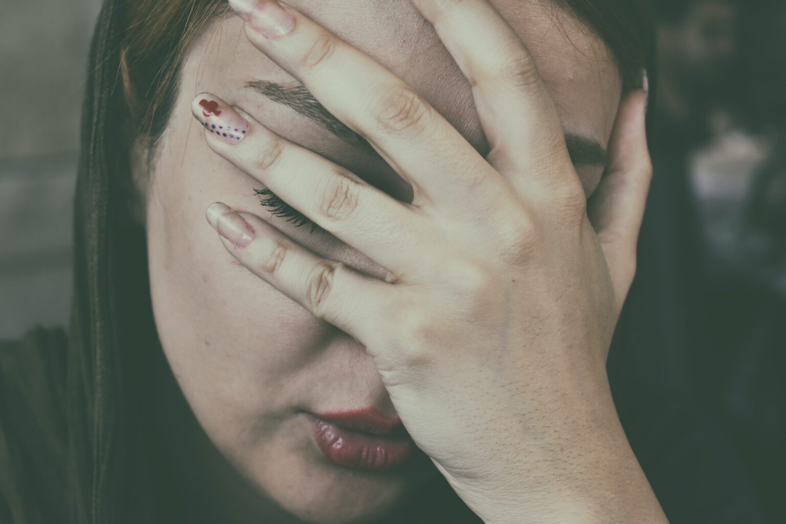 A woman with painted nails covering her face with one hand, displaying a sense of distress or fatigue after a long visit at the Dallas dentist office.