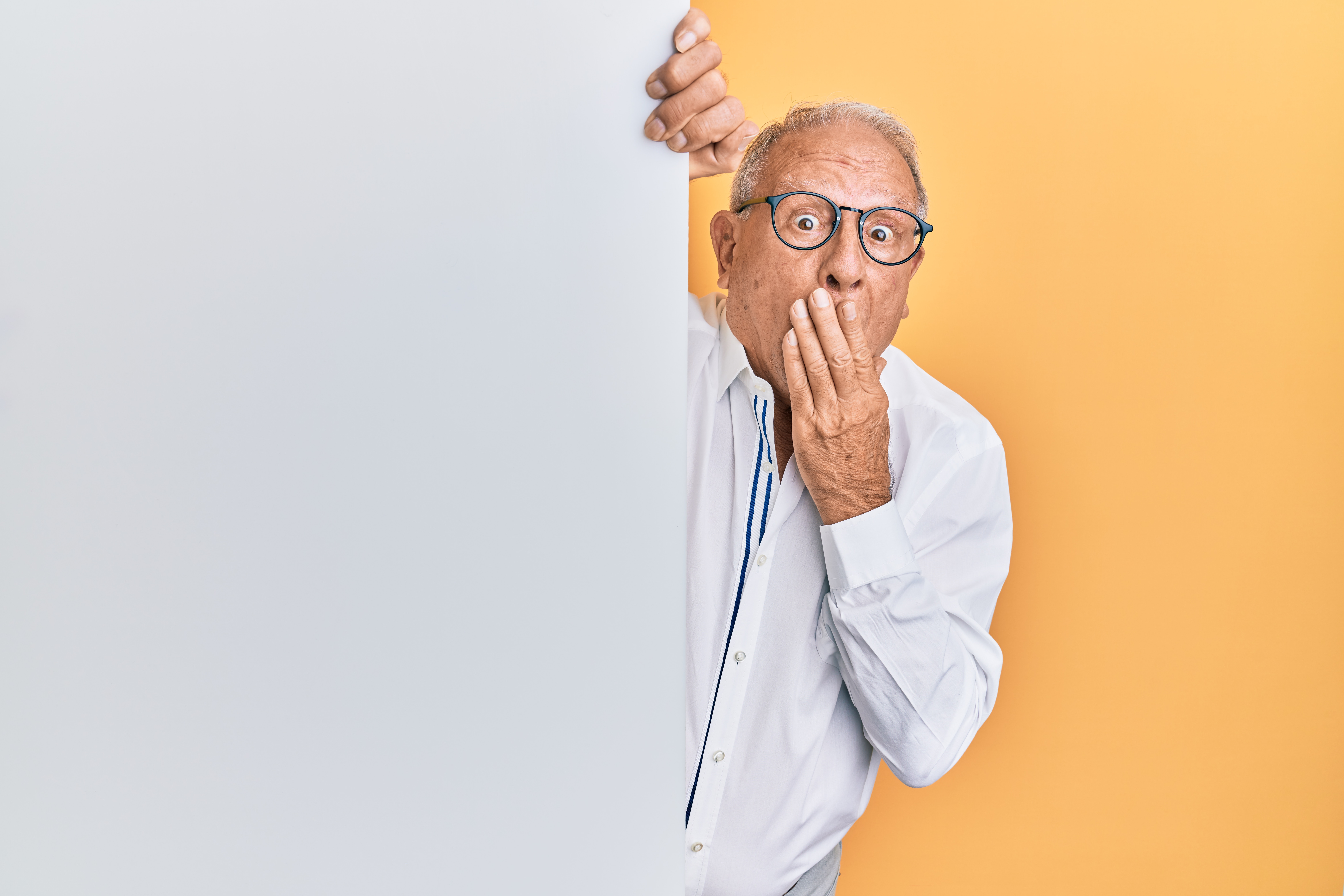 Older man peeks out from behind a wall, indicating his anxiety surrounding an upcoming Dallas teeth cleaning