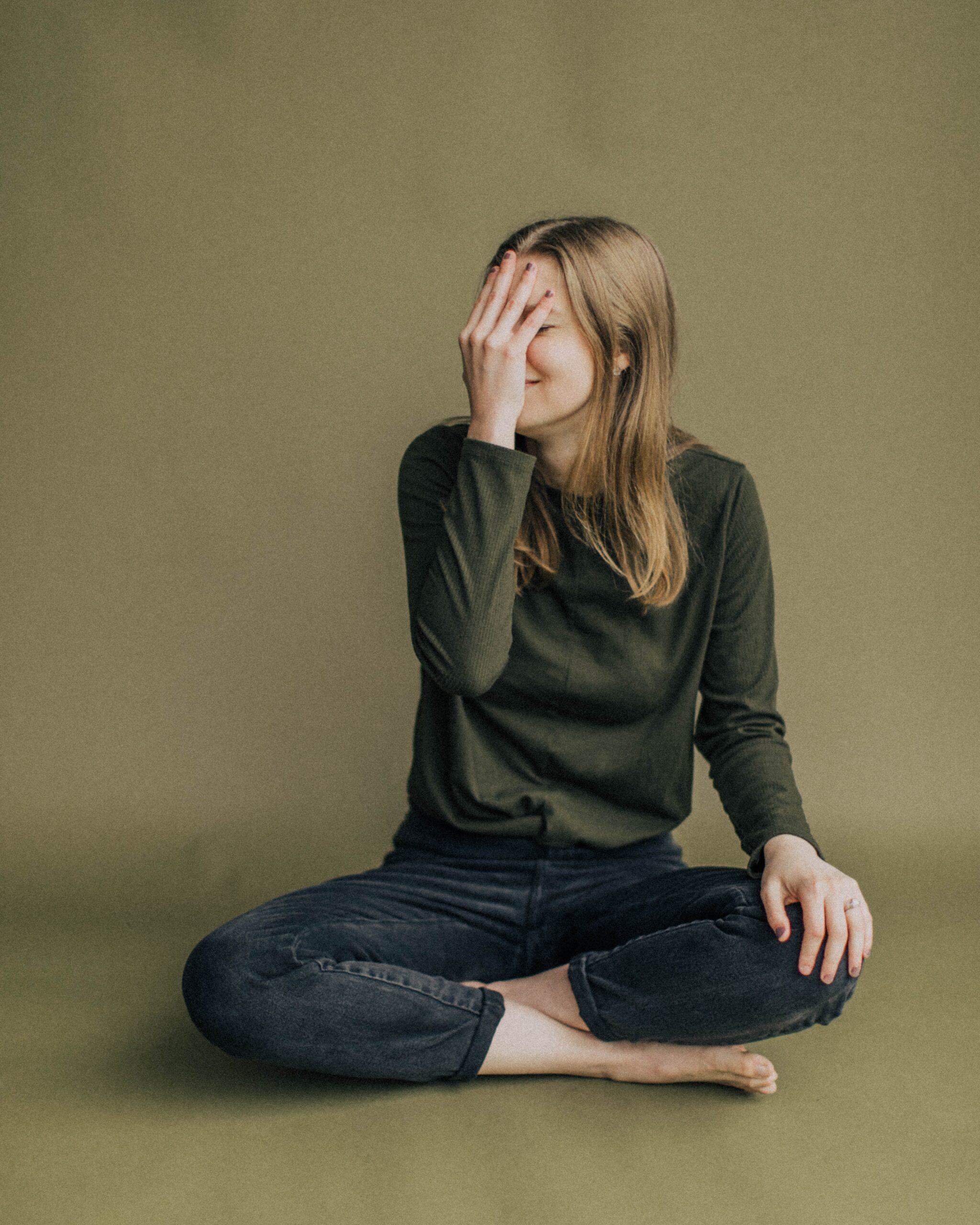 Woman sitting on the floor with her hand covering her face, contemplating her next visit to an affordable Dallas dentist.