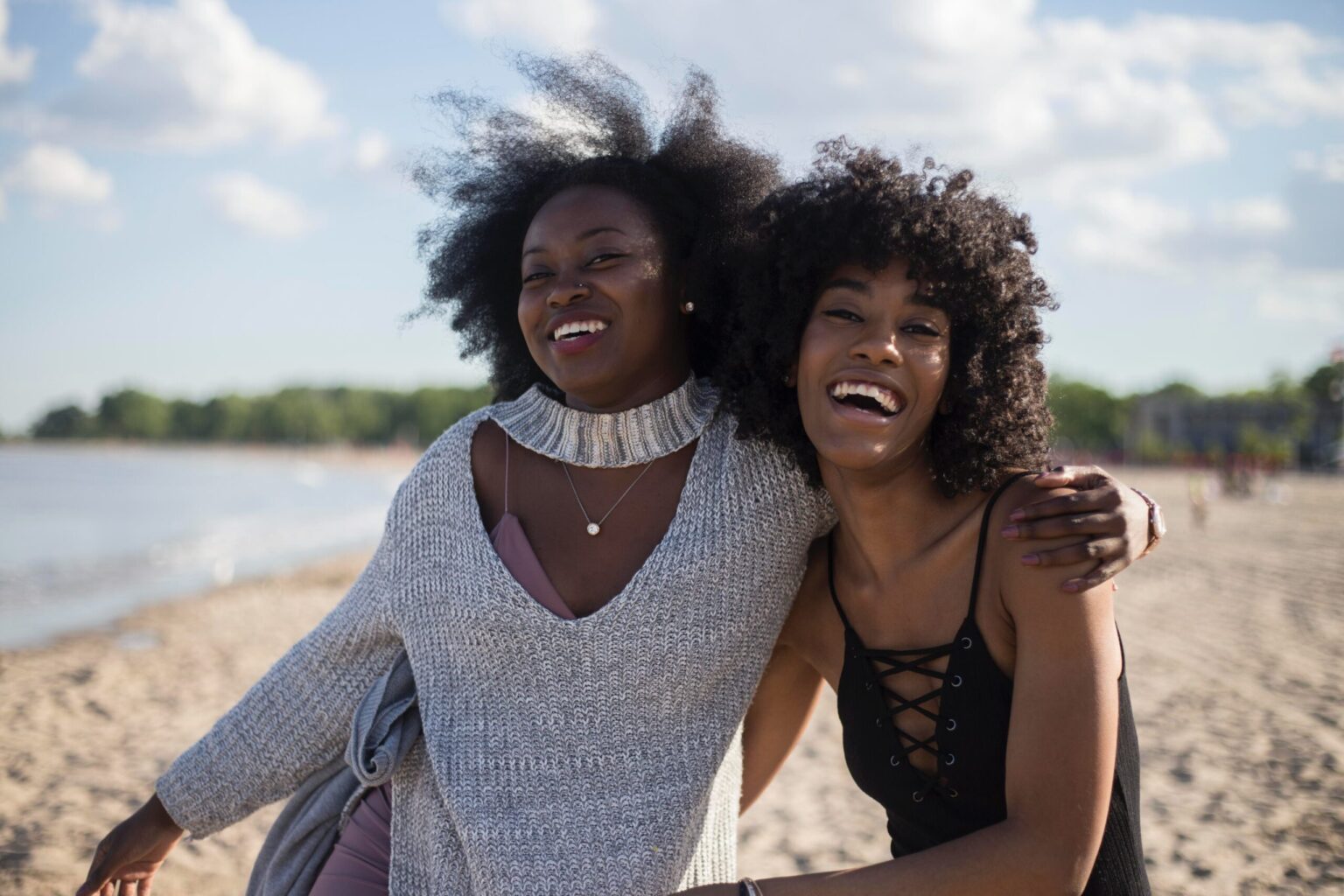 Two women smiling, showcasing their dentist-approved bright smiles, and embracing each other on a beach.