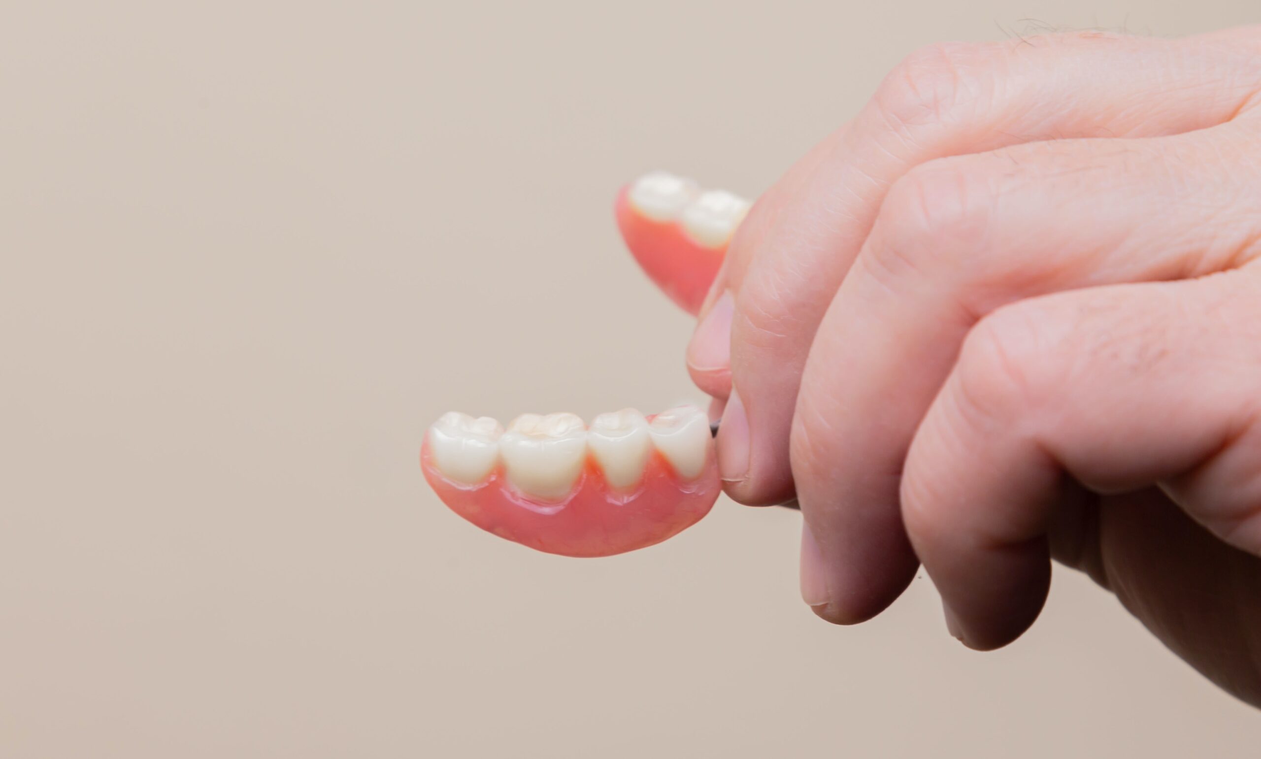 A hand holding a set of upper dentures against a neutral background in a dental office.