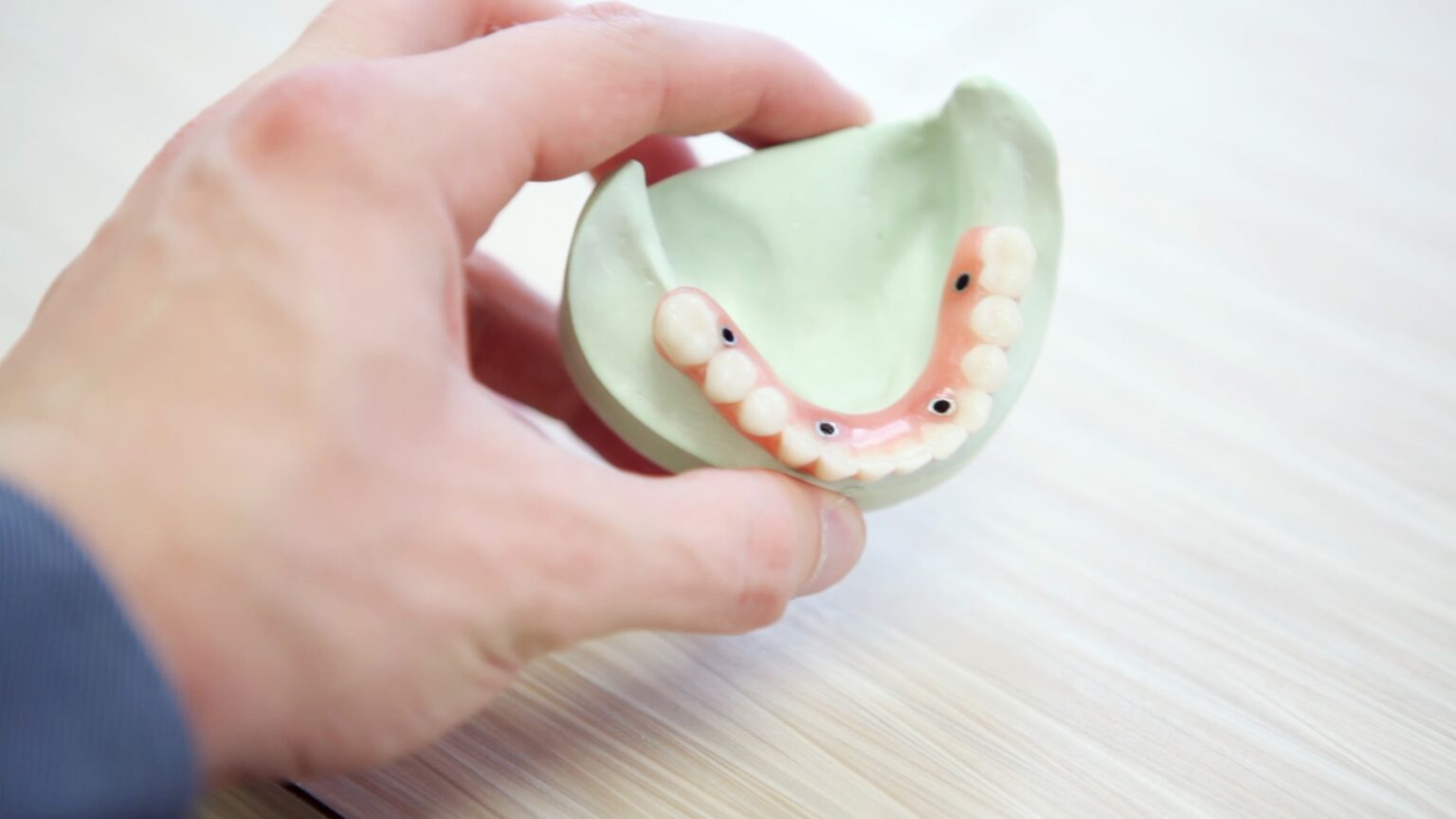 A person holding a set of dentures inside a dental model at an affordable Dallas dentist office.