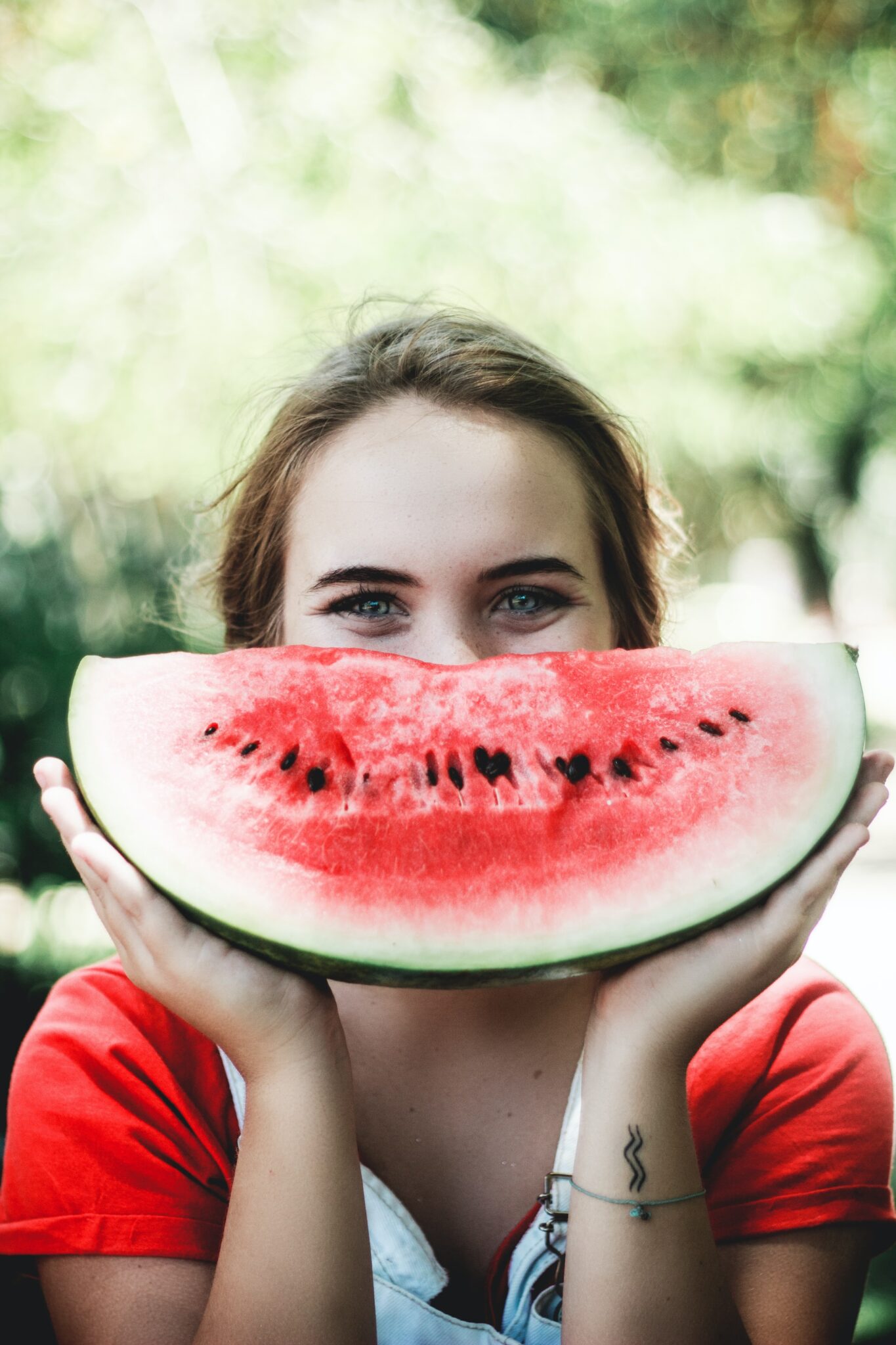A woman holding a slice of watermelon up to her face, her eyes peeking over the top, pictured in a bright dental clinic.