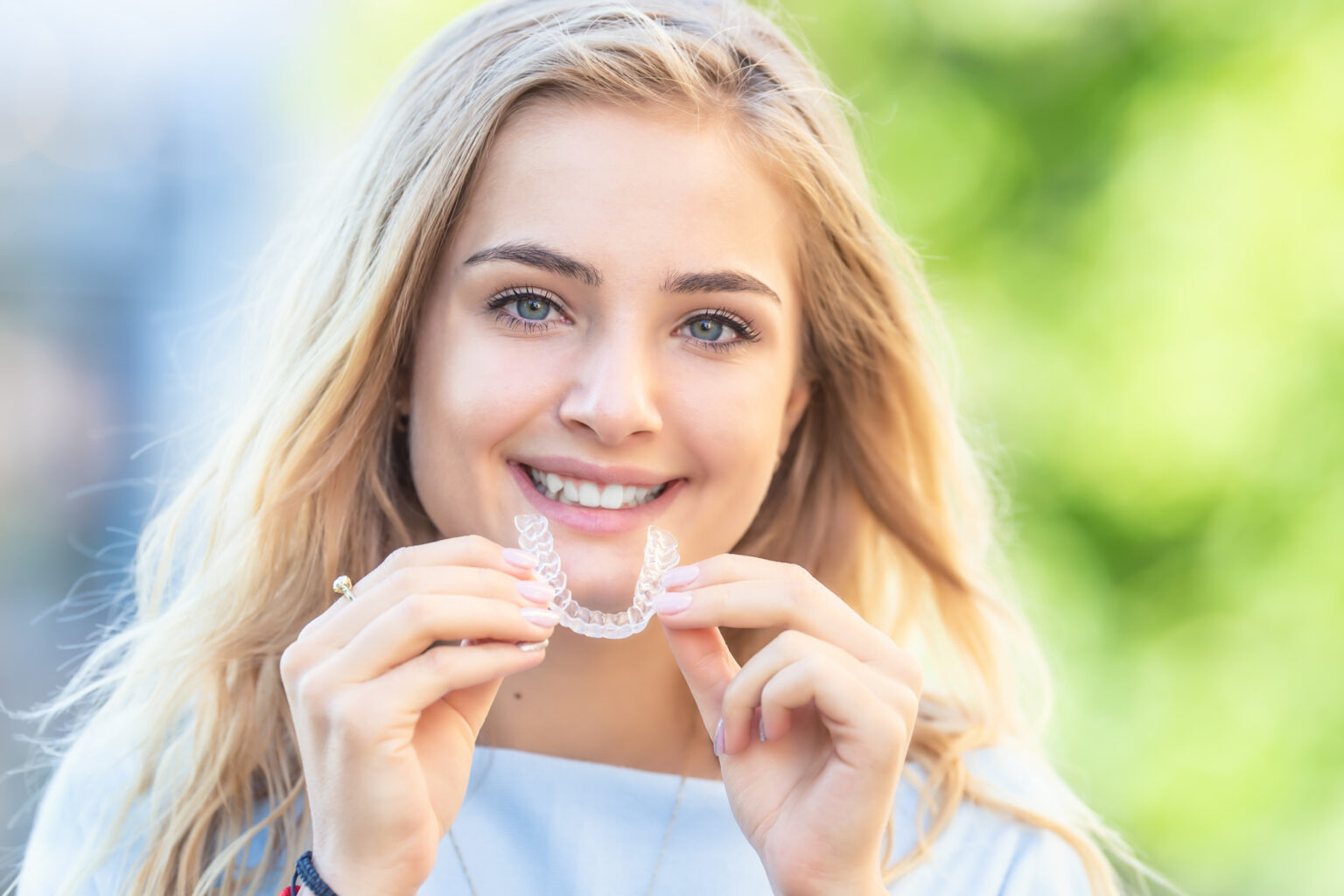 Young woman smiling and holding clear orthodontic aligners from an affordable Dallas dentist.