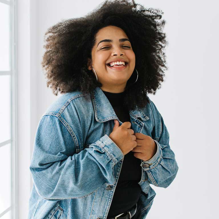 A joyful woman in a denim jacket laughing with closed eyes at the dental office.