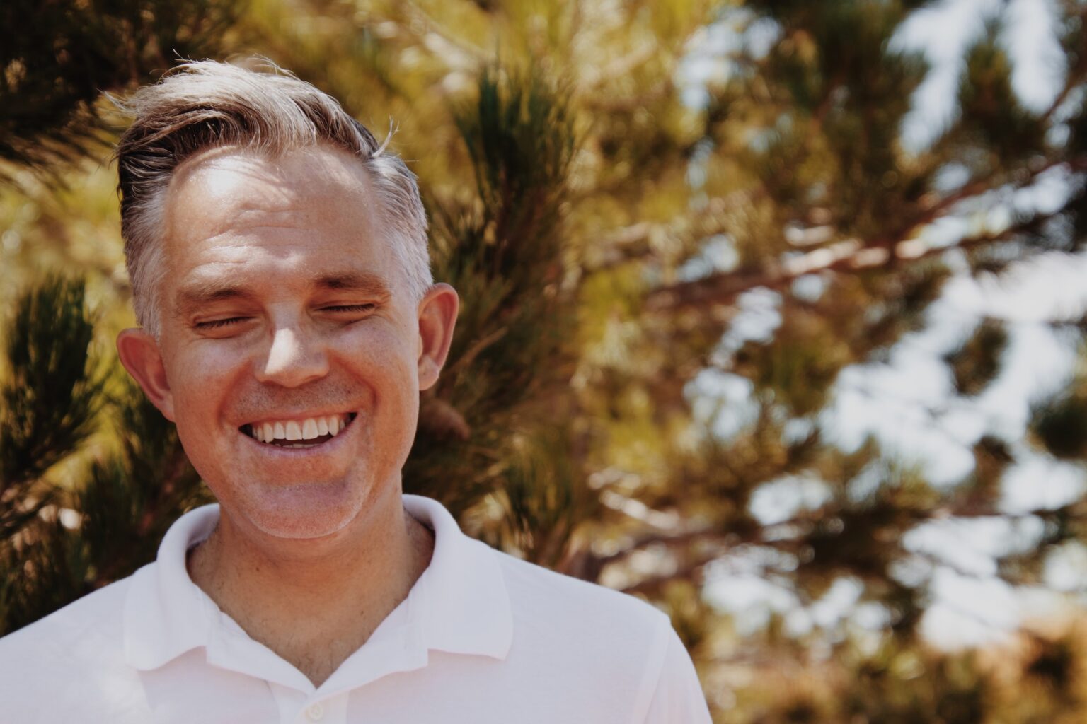 Smiling man with grey hair, resembling an affordable Dallas dentist, wearing a white shirt outdoors.