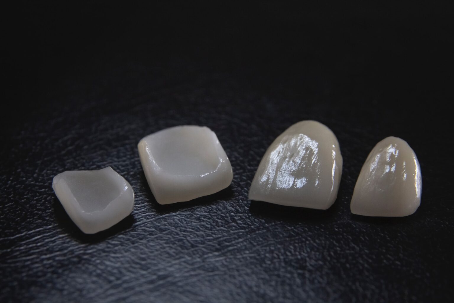 Four affordable dental veneers on a dark surface.