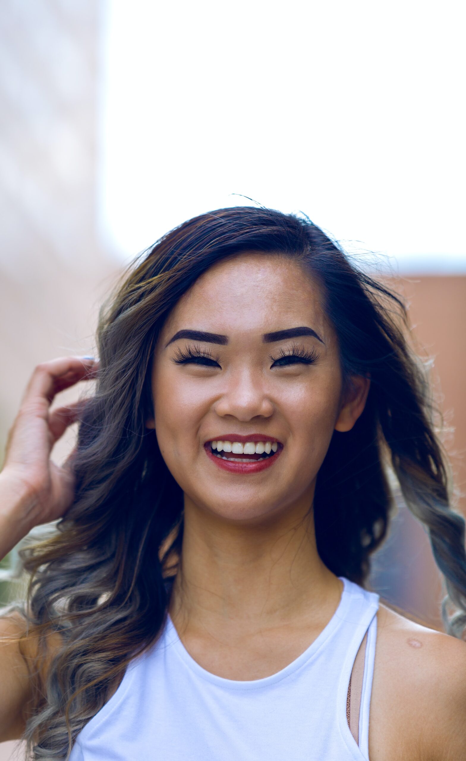 A smiling woman with long, curled hair touching her hair lightly after visiting an affordable Dallas dentist.