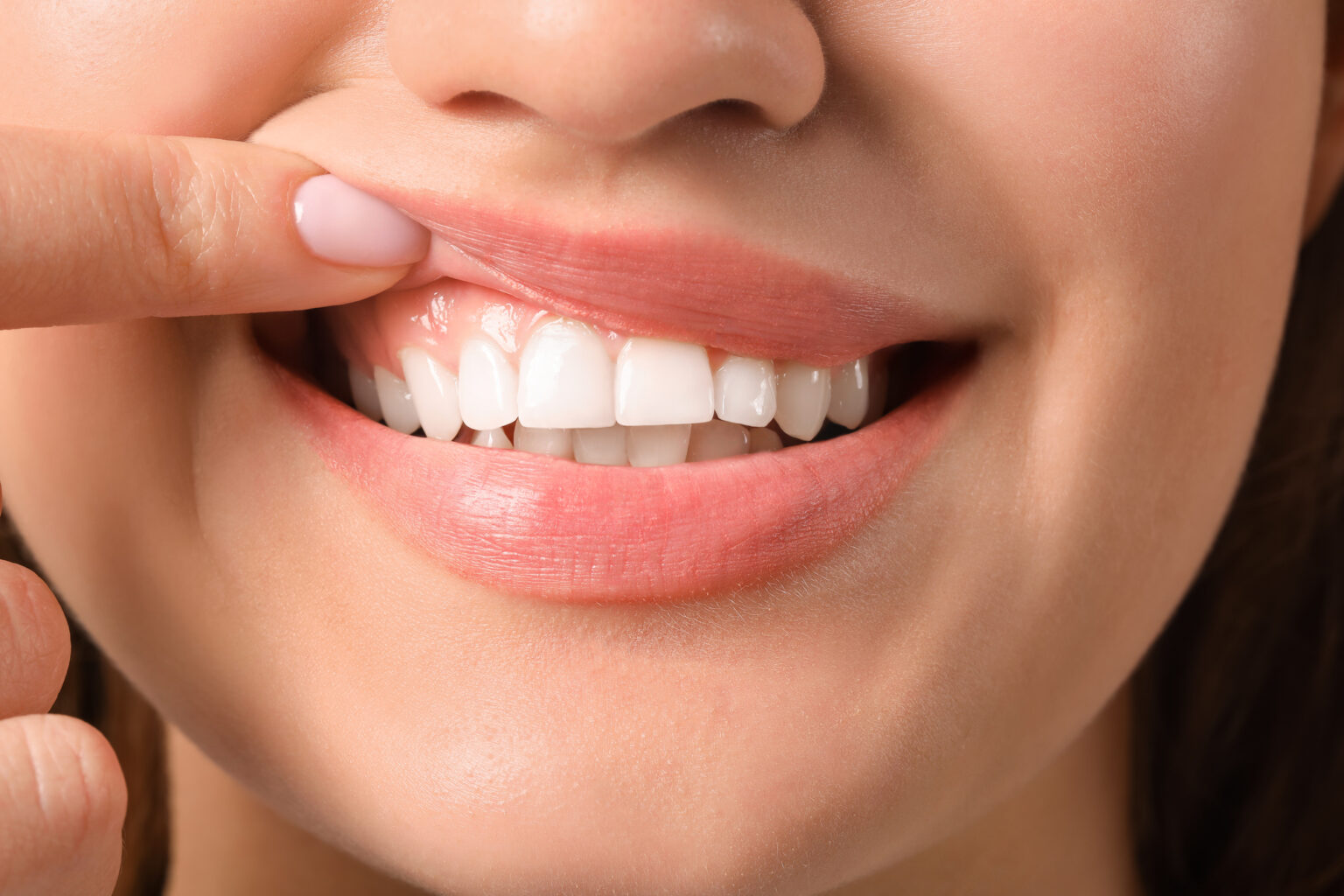 Close-up of a smiling person with their finger on their lips at an affordable Dallas dental clinic.