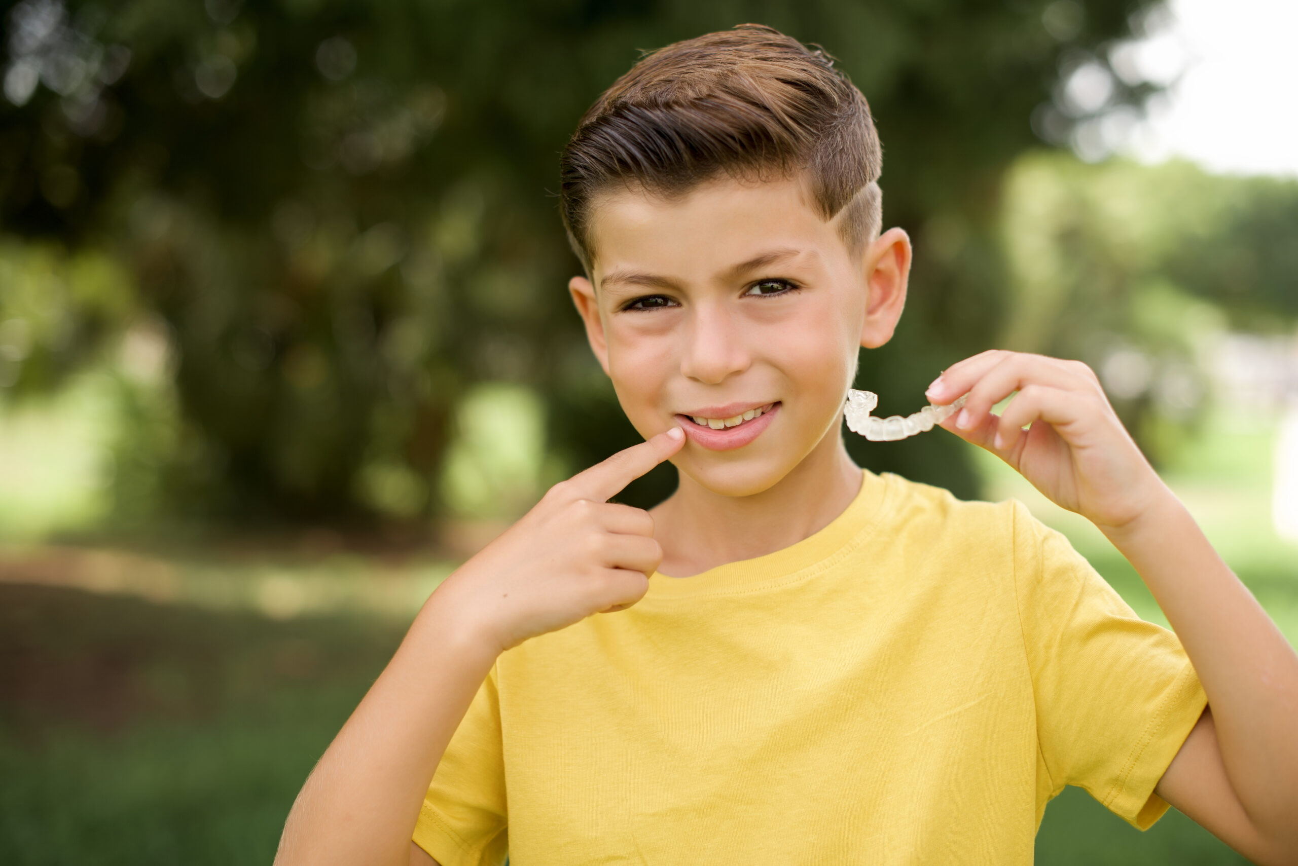 A boy in Texas pointing to his smile while holding an invisible aligner.