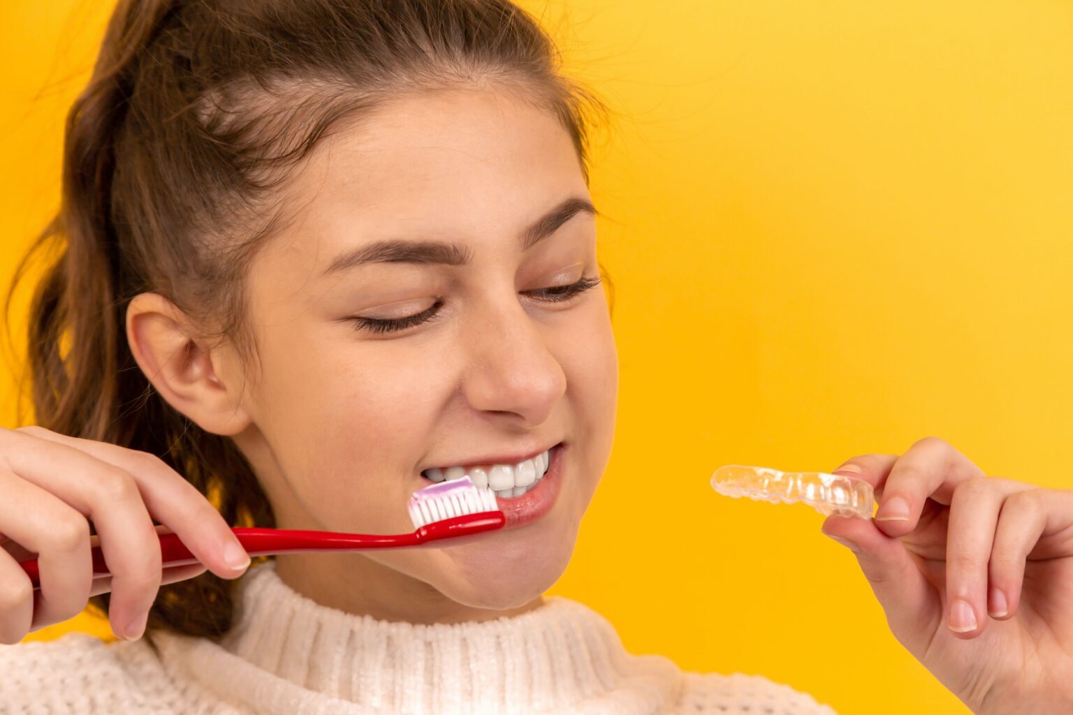 Young woman brushing teeth in a Texas dentistry while holding clear dental aligners.