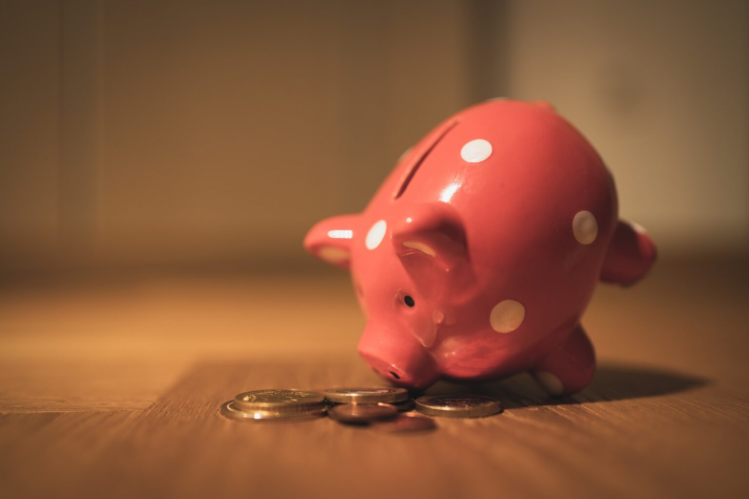 A pink, polka-dotted piggy bank lying on its side with coins scattered in front of it, resembling the playful decor one might find in a Texas dentistry waiting room.