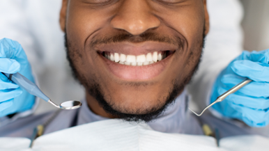 A patient smiling while a dentist in a Texas dentistry clinic performs an examination with dental instruments.