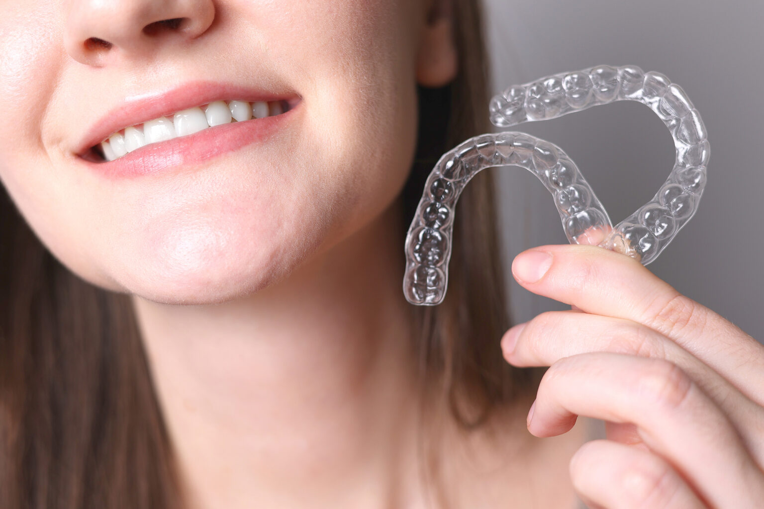 Woman holding clear dental aligners near her smile at an affordable Dallas dental clinic.