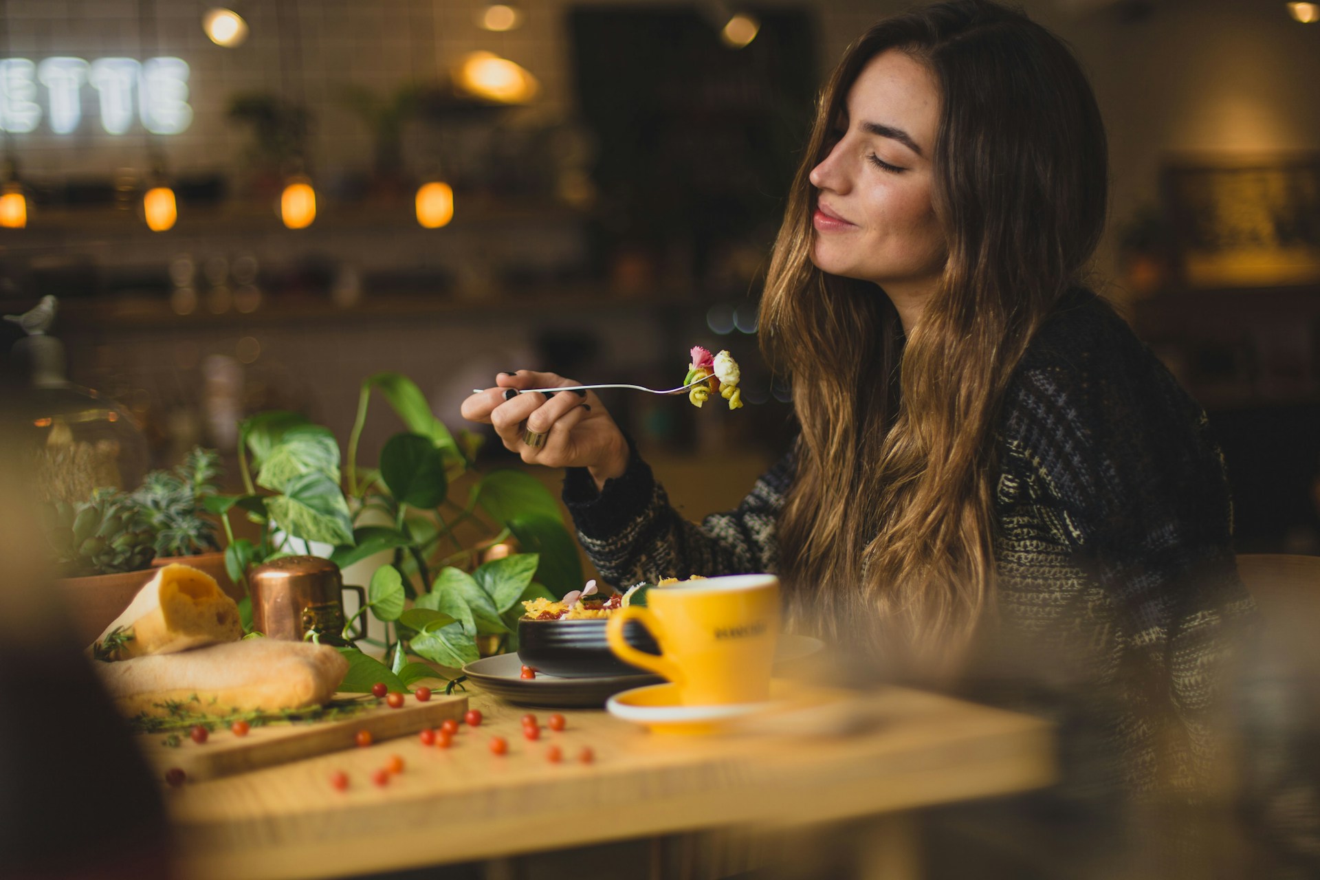 Woman enjoying a meal in a cozy cafe, smiling as she eats a salad, with a cup of coffee and bread on the table.