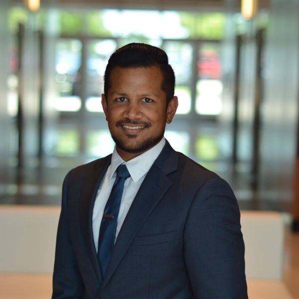 A professional man in a blue suit and tie smiling in a modern office lobby.