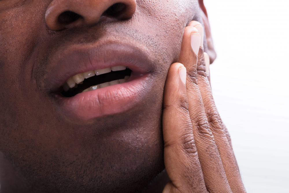 Close-up of a person holding their cheek, mouth slightly open, possibly indicating dental pain or discomfort—time to visit a trusted dentist in Dallas, TX.