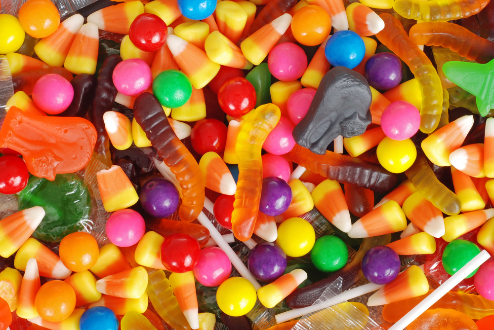 A colorful assortment of Halloween candy, including candy corn, gumballs, gummy worms, lollipops, and various shaped gummies, all mixed together in a festive display.