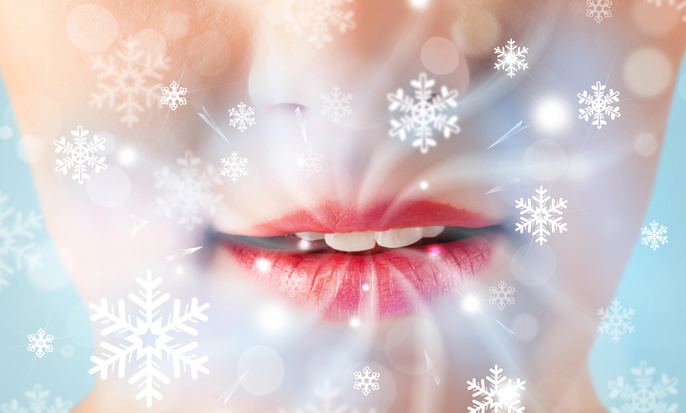 Close-up of a person's lips with a soft pink tint, surrounded by an overlay of white snowflakes and a frosty, dreamy effect, suggesting a winter or cold theme.